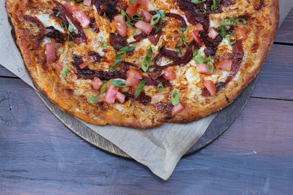 Thin crust pizza topped with bacon and chicken sitting on wooden table