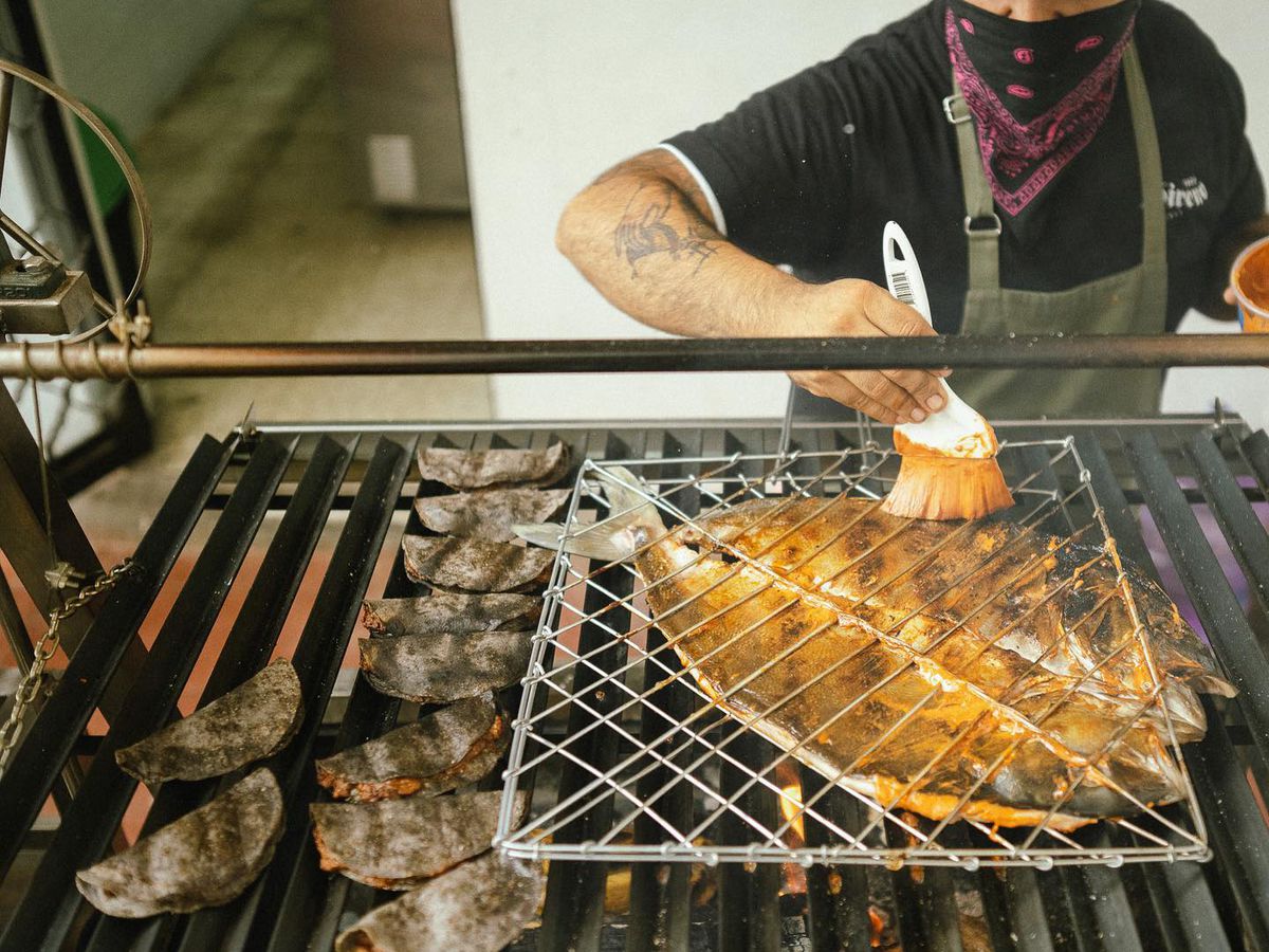A cook brushes sauce on a fish pressed to a grill by a steel grate