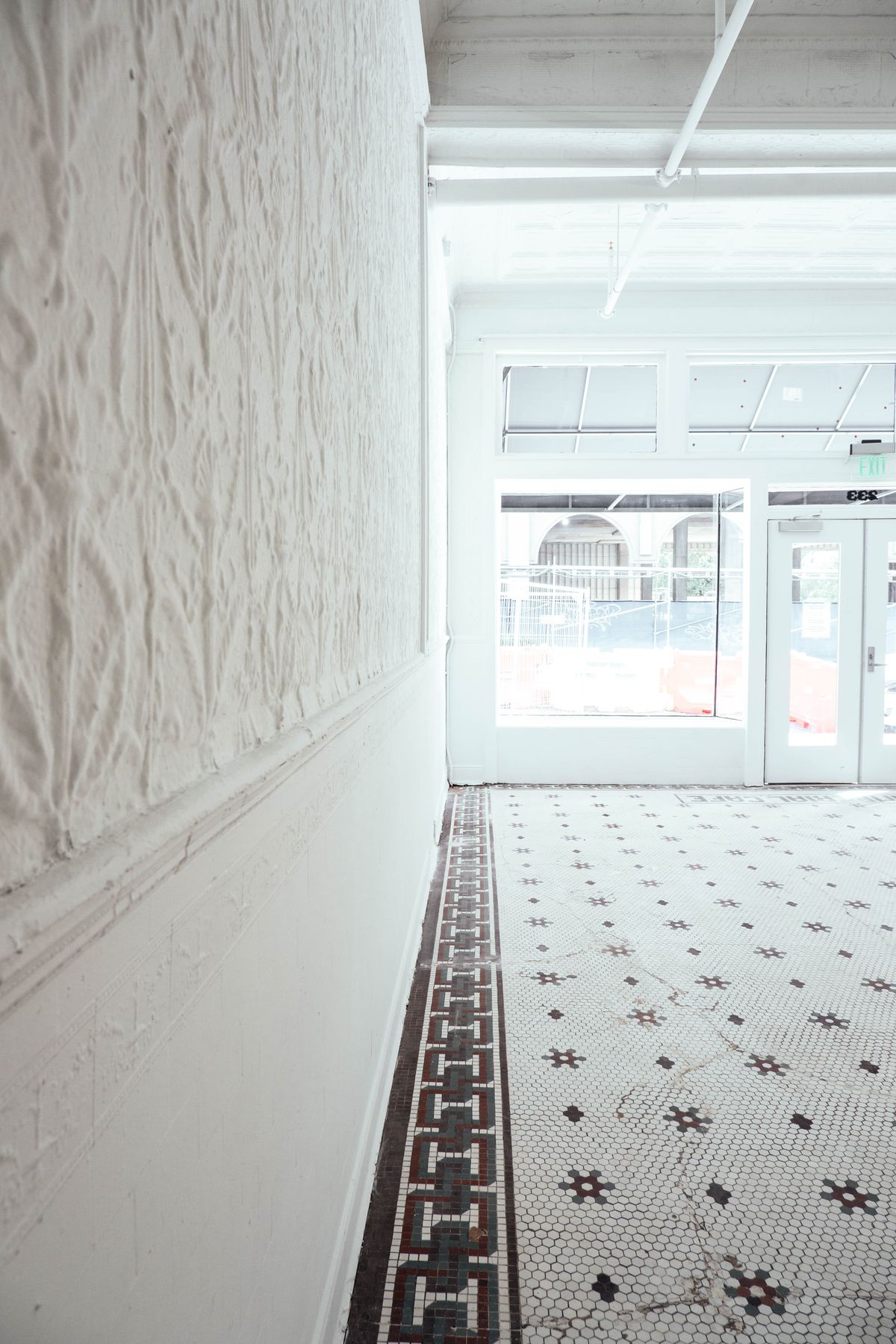 A view toward the storefront from the back of the future location of Spiller Park Coffee in downtown Atlanta, with the old brown and white decorative tile floor and whitewashed walls. 