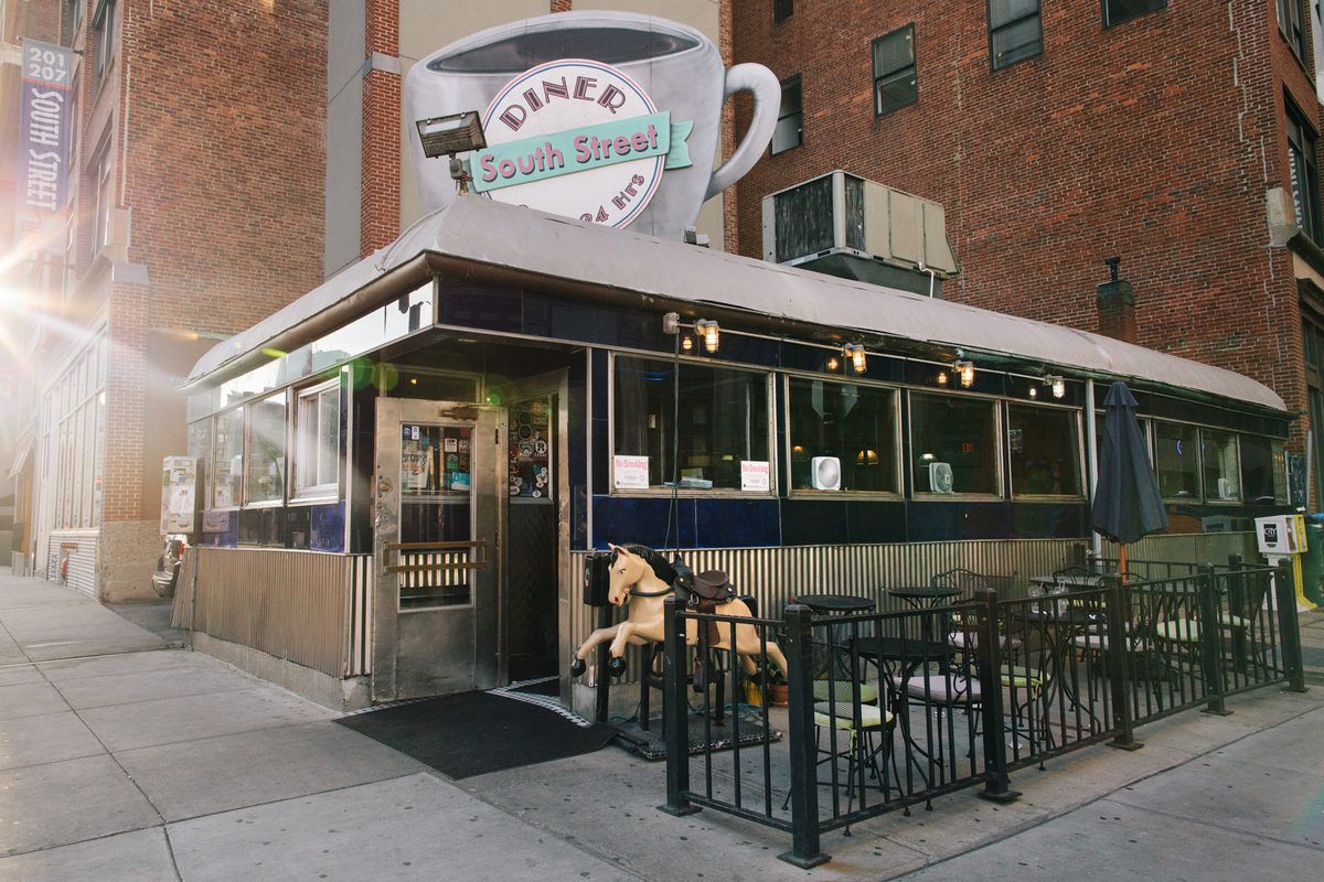 Daytime exterior view of Boston’s South Street Diner with its iconic coffee cup-shaped sign and metal siding. A carousel horse sits by the door.
