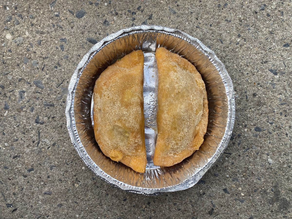 Two brown empanadas sit in a silver aluminum container with their flat sides facing each other