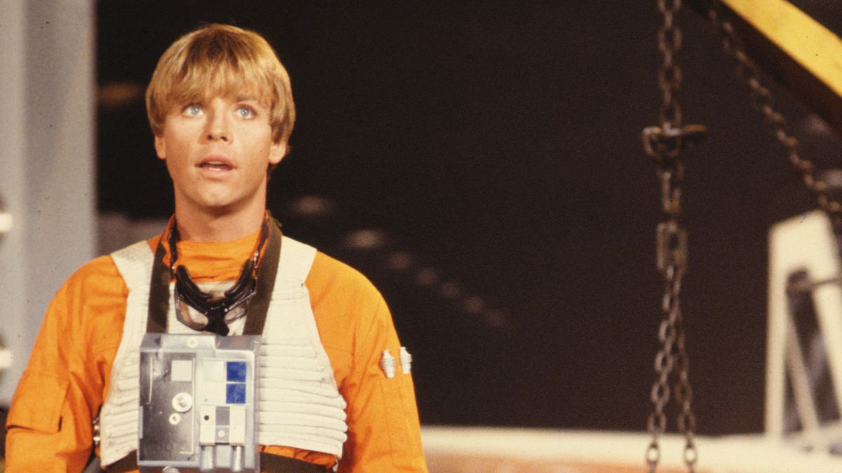 A young Mark Hamill as Luke Skywalker stands in orange-and-white X-wing pilot gear, his mouth hanging open a bit gormlessly, in a shot from The Star Wars Holiday Special