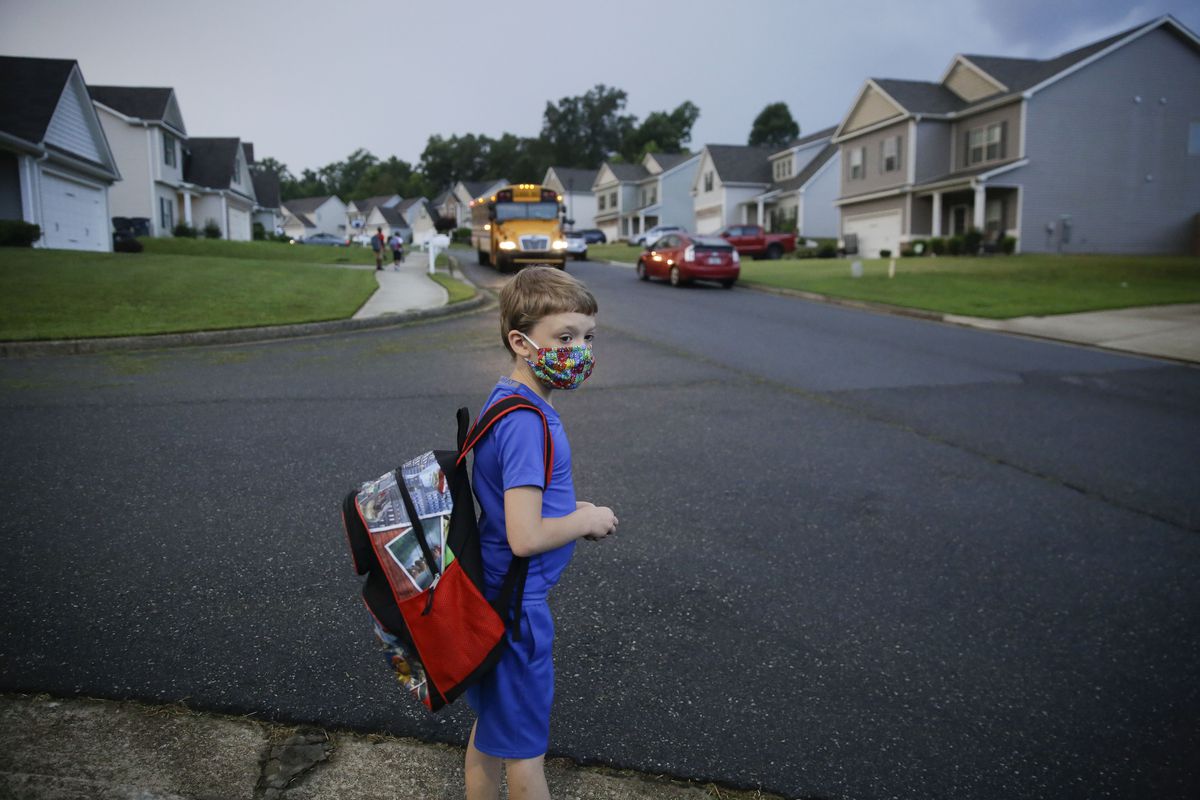 In this Aug. 3, 2020, file photo, Paul Adamus, 7, waits at the bus stop for the first day of school in Dallas, Ga. 