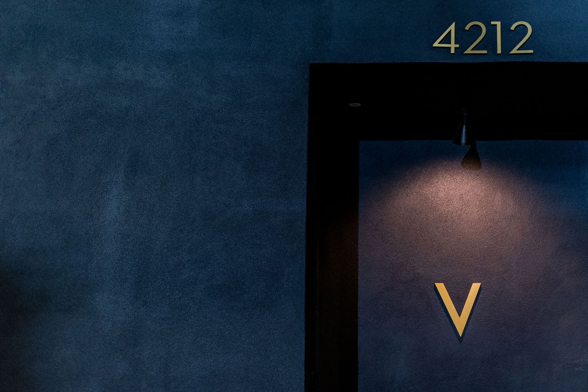 The dark blue exterior of a restaurant with a single V sign on the door.