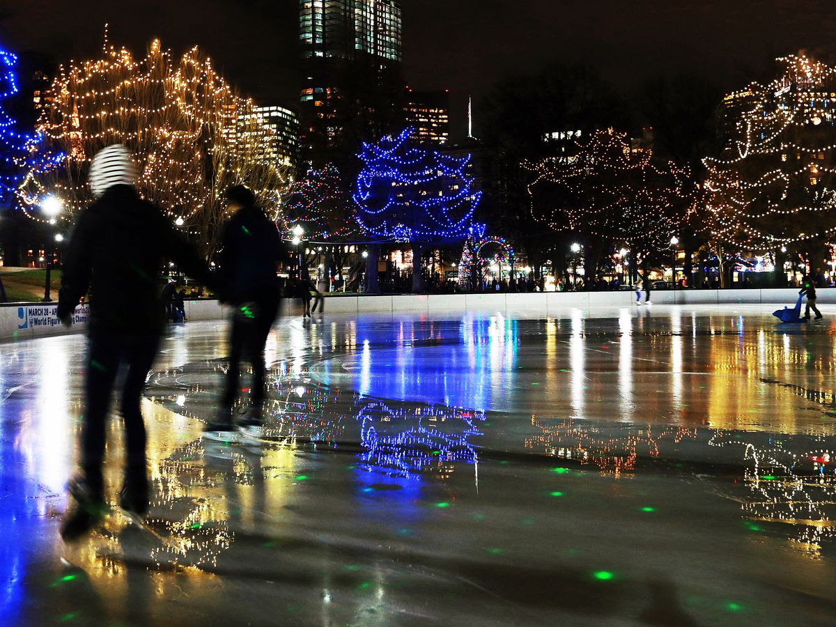 People ice-skating at night, surrounded by illuminated trees.
