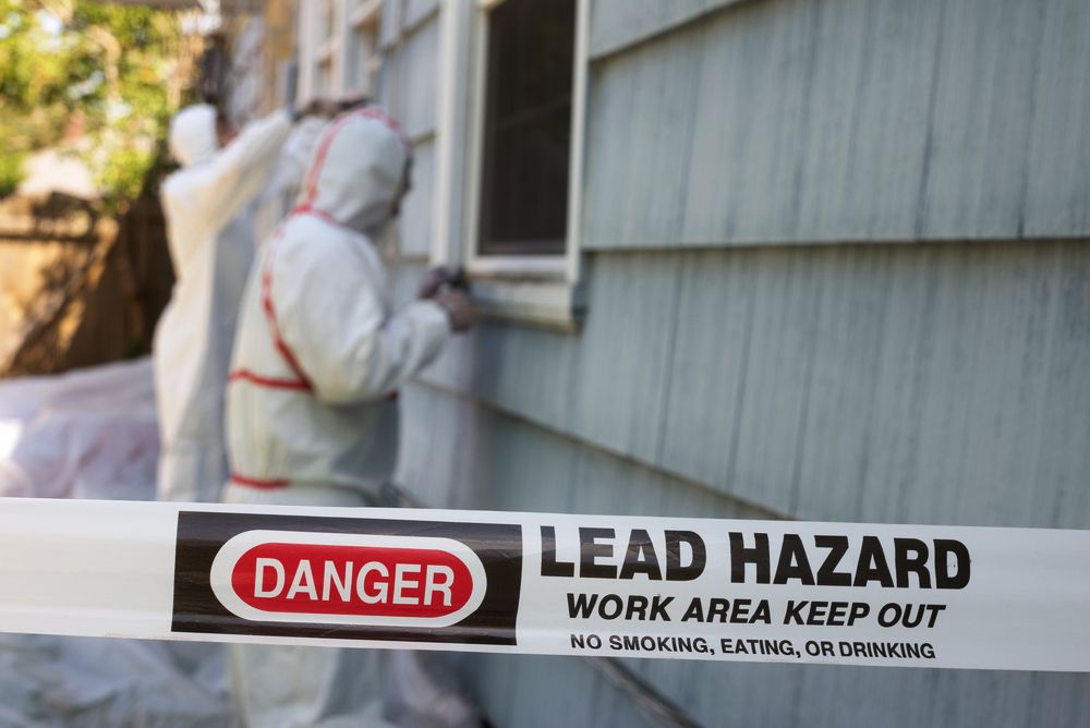 Workers in hazmat suits stripping lead paint from the side of a house.