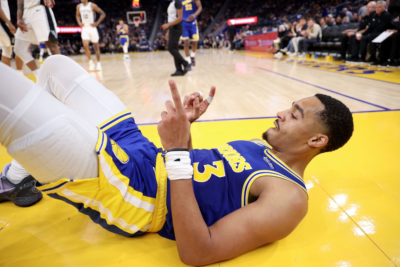 Jordan Poole laying on his back with finger guns 