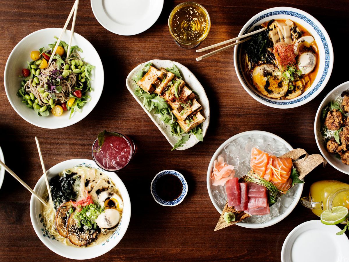 A table spread with Japanese dishes like ramen and sashimi and small bowls of soy sauce. 