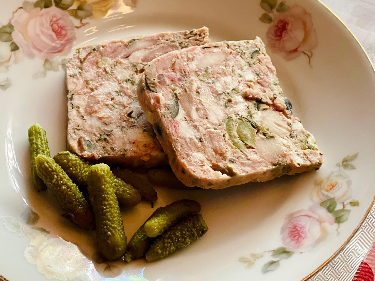 Slices of terrine on a floral-decorated plate with pickles.