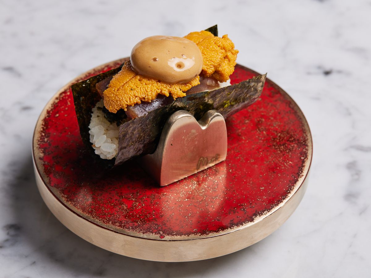 Uni lies above tuna in this hand roll, which sits on an ornamental red holder