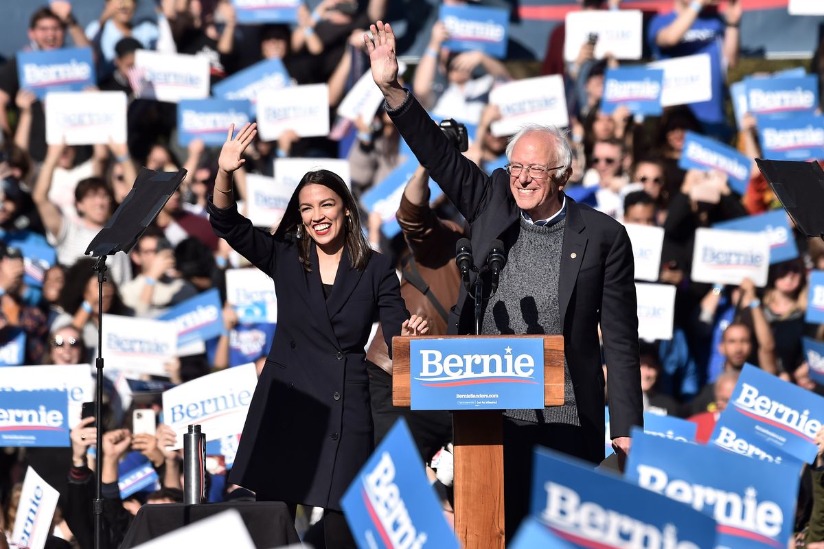 Senator Bernie Sanders and Representative Alexandria Ocasio-Cortez wave amid a sea of “Bernie for president” signs.