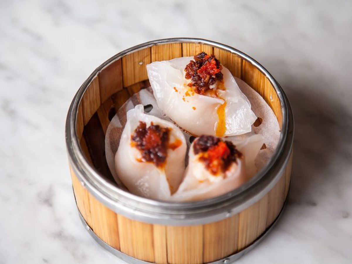 A round Chinese bamboo steamer that holds three shrimp dumplings topped with red chili crisp.