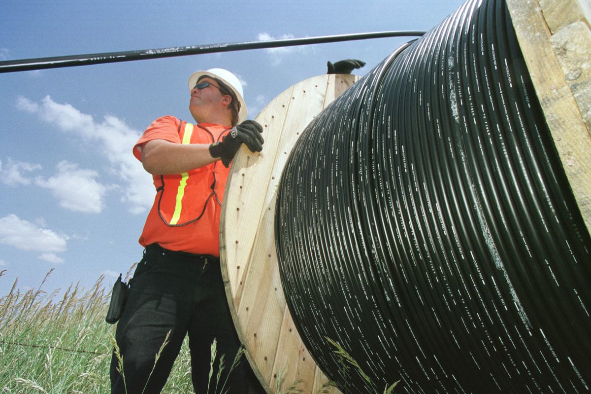 Fiber-optic cable on a huge spool, being overseen by a hard-hatted worker