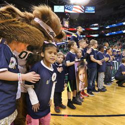 Children living with chronic and debilitating rare diseases or their surviving siblings, who will carry a portrait in memory of a loved one, stand with members of the Utah Jazz and the San Antonio Spurs during the national anthem prior to Monday's game. They are wearing lapel pins and wristbands from the National Organization for Rare Disorders in Salt Lake City.  
