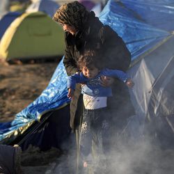 A woman holds a child next to a fire at the northern Greek border point of Idomeni, Greece, Sunday, March 20, 2016. German Chancellor Angela Merkel is urging migrants in the squalid tent city at Idomeni, on the Greek-Macedonian border, to trust Greek authorities and leave for better accommodation as thousands are still staying on site after the closure of Macedonia's border. 