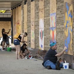 Members of the community paint over the boarded up windows of businesses near 57th Street and 7th Avenue as the city of Kenosha prepares fo the fourth day of civil unrest after police shot Jacob Blake, Wednesday evening, Aug. 26, 2020.