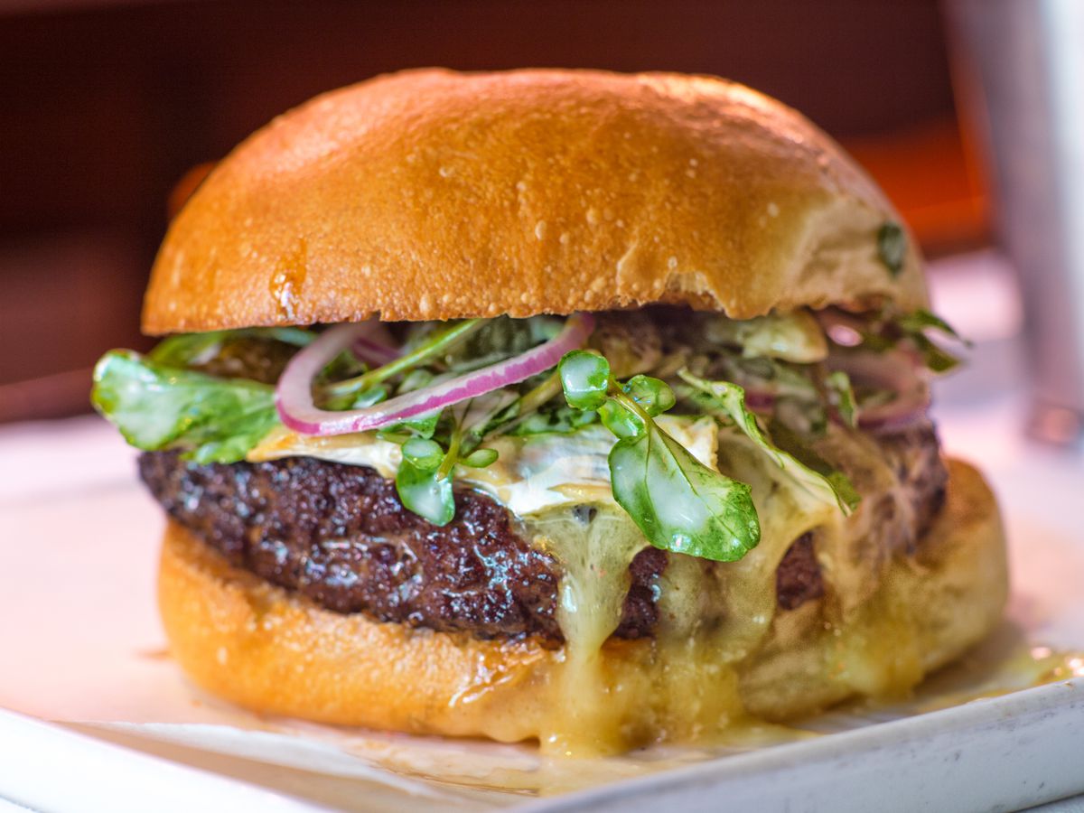 A burger topped with melted Saint-Andre cheese, watercress, onions, and cornichons.
