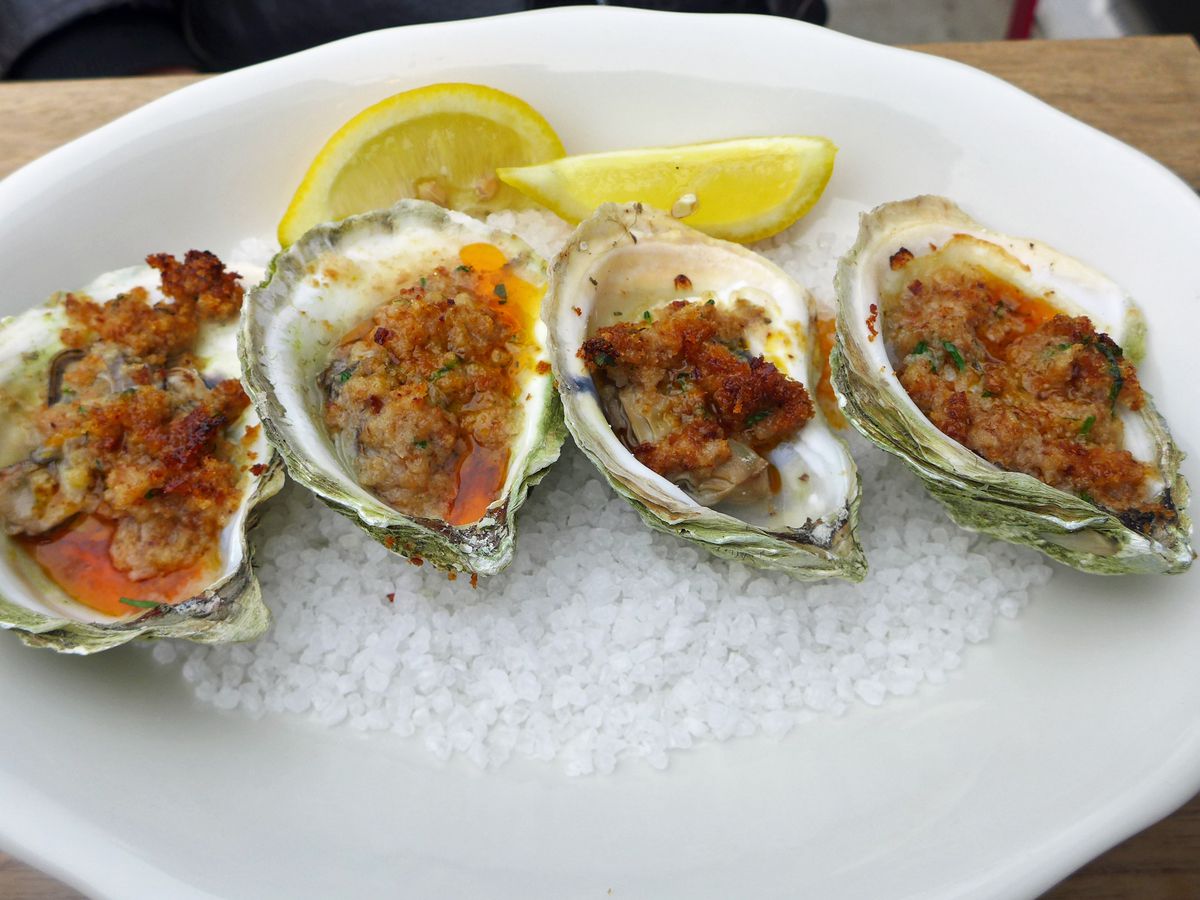 Four roast oysters with crumbs and lemon on the side.