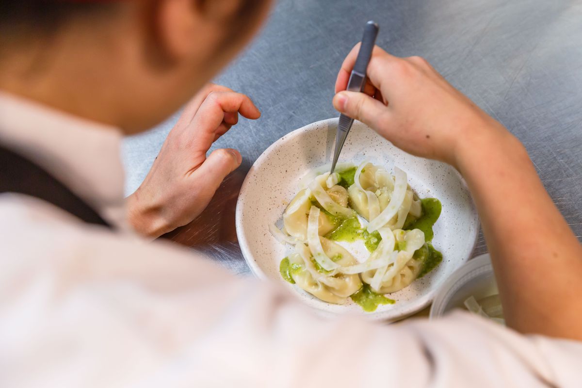 A woman holds tweezers and adds onions to a bowl of dumplings
