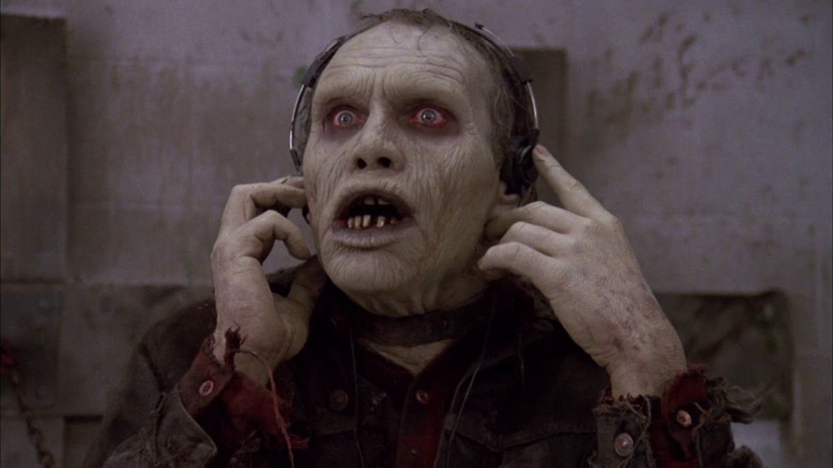 A zombie wearing a collar gives a look of surprise while listening to music in over-ear headphones in George Romero’s Day of the Dead.