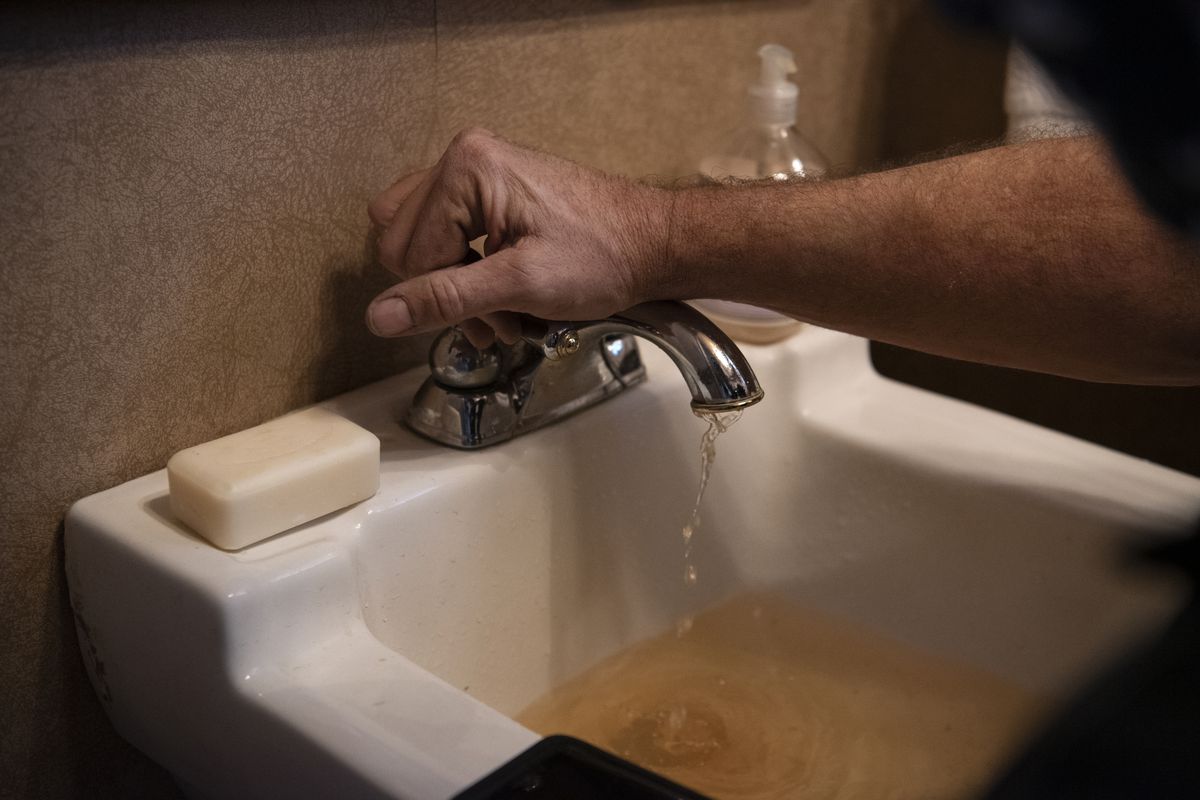 A technician repairs a sink with brown tap water