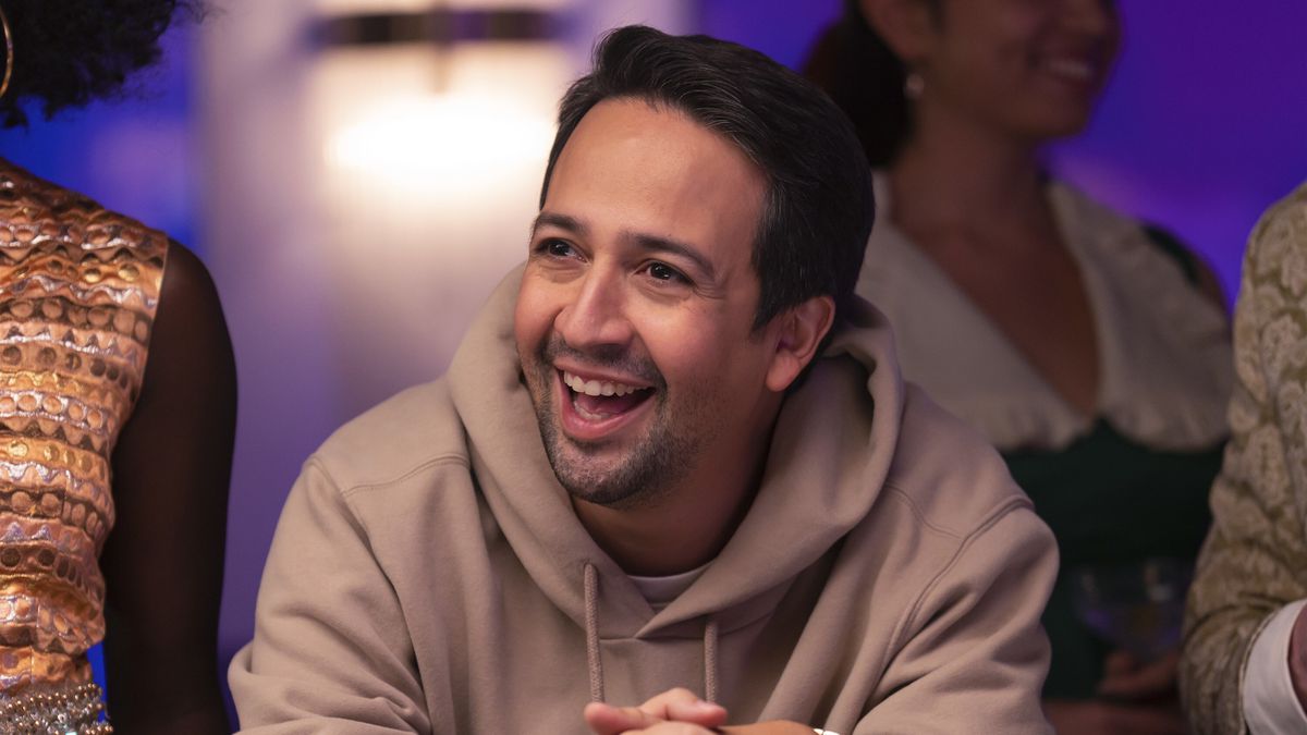 Lin-Manuel Miranda as Hermes, leaning over a poker table with a big goofy smile