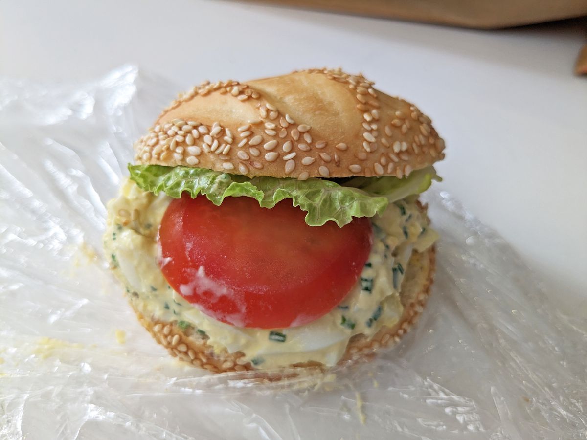 A round roll with sesame seeds, its plastic wrap around it.