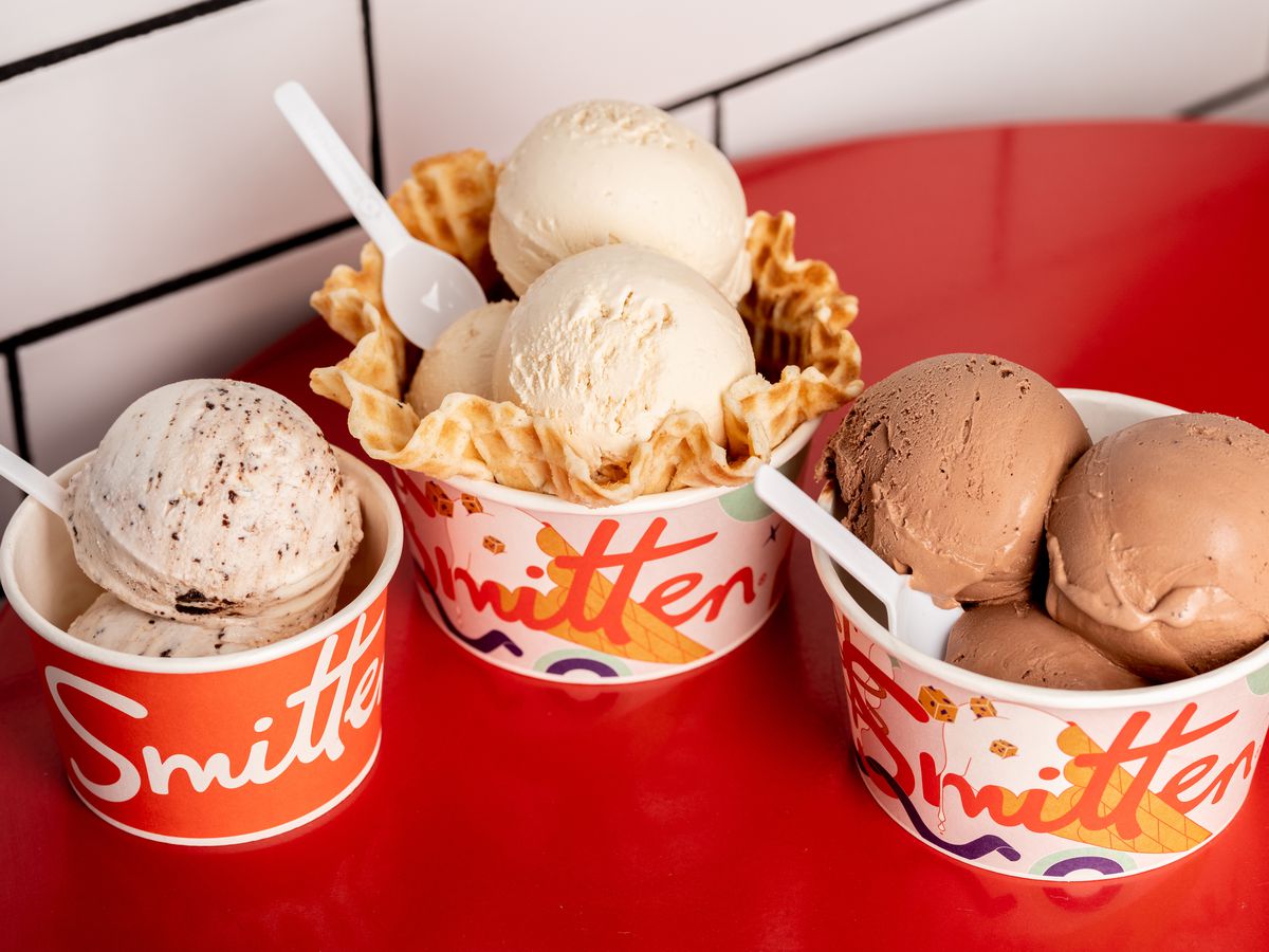 Three cups of ice cream with multiple scoops in each. The middle cup has a waffle bowl in it, and all three have white plastic spoons.