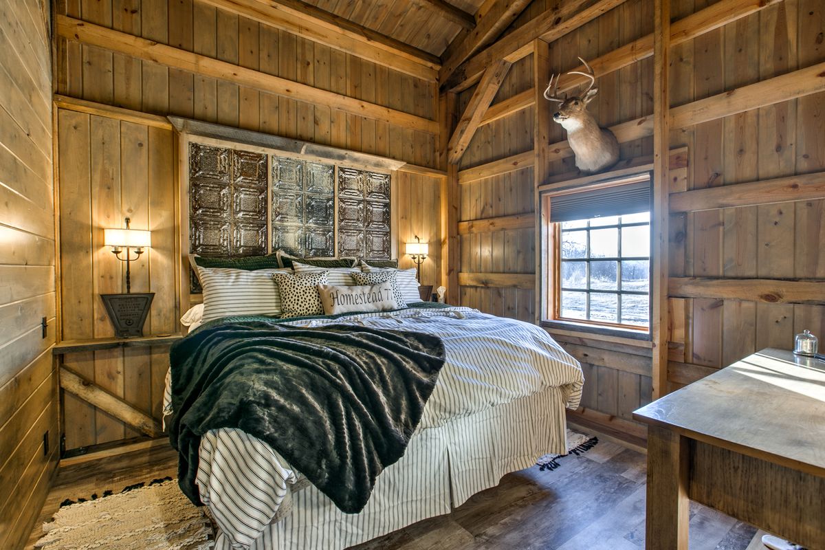 A rustic bedroom with a striped bed, taxidermy deer, and exposed wood.