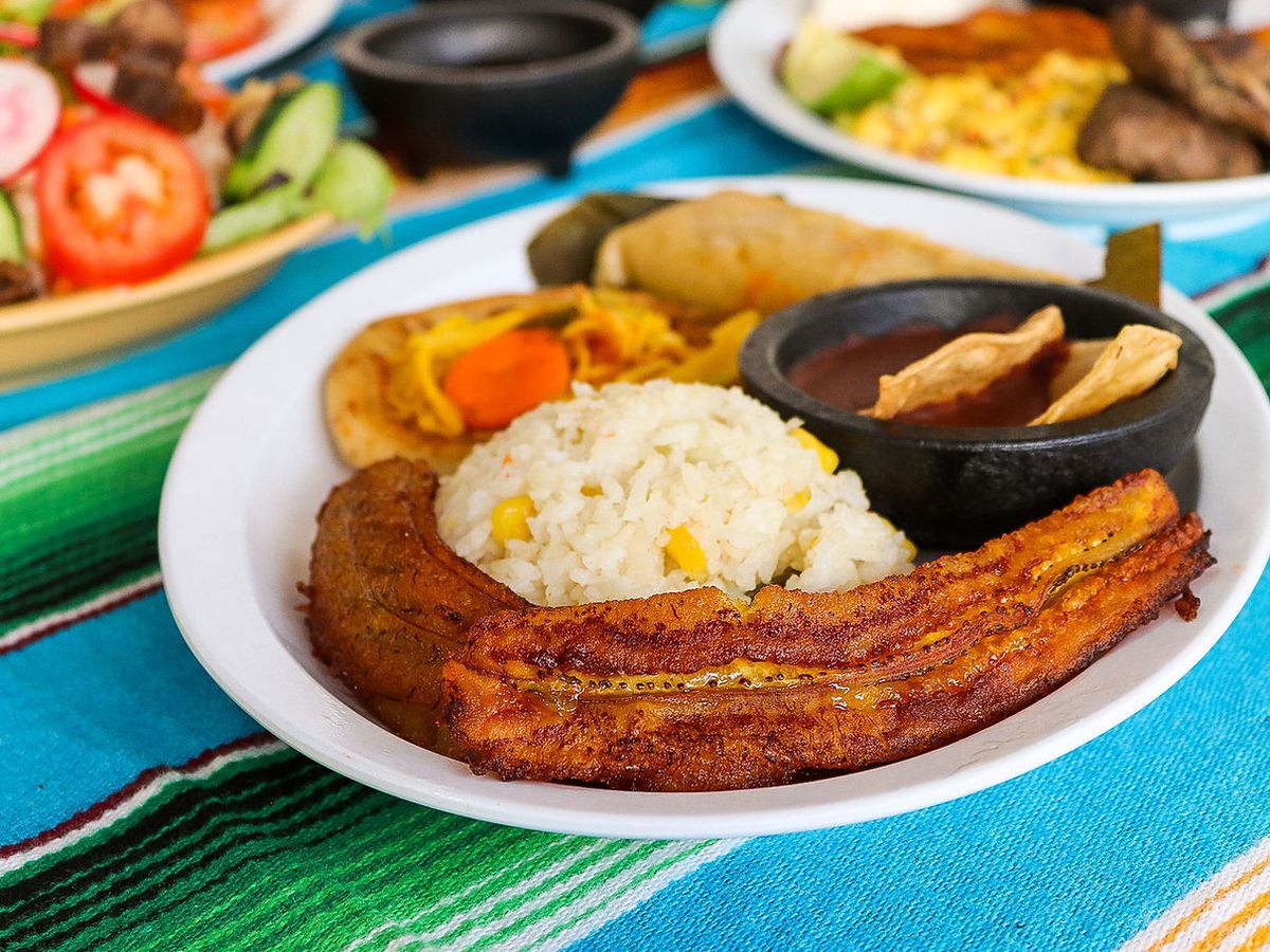 A white plate with rice, a long plantain, salsa, and vegetables. 