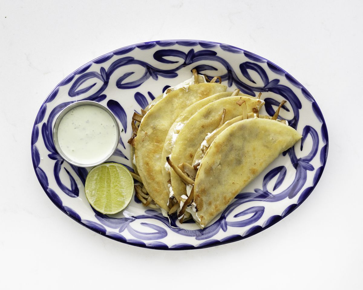 A blue-and-white plate with three tacos, a slice of lime, and a white dressing on the side.