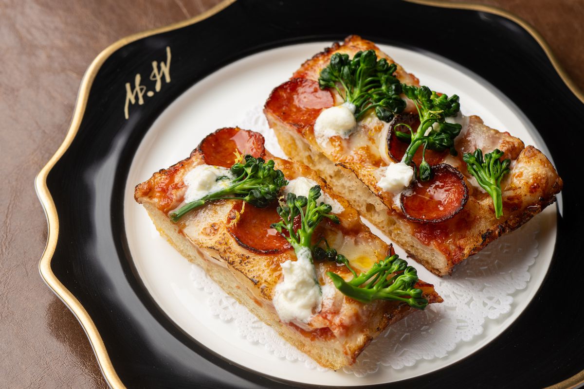 Two small rectangles of pizza dough with pepperoni and broccoli on top set on a black and white fine dining plate at new LA restaurant Mr. Wanderlust.