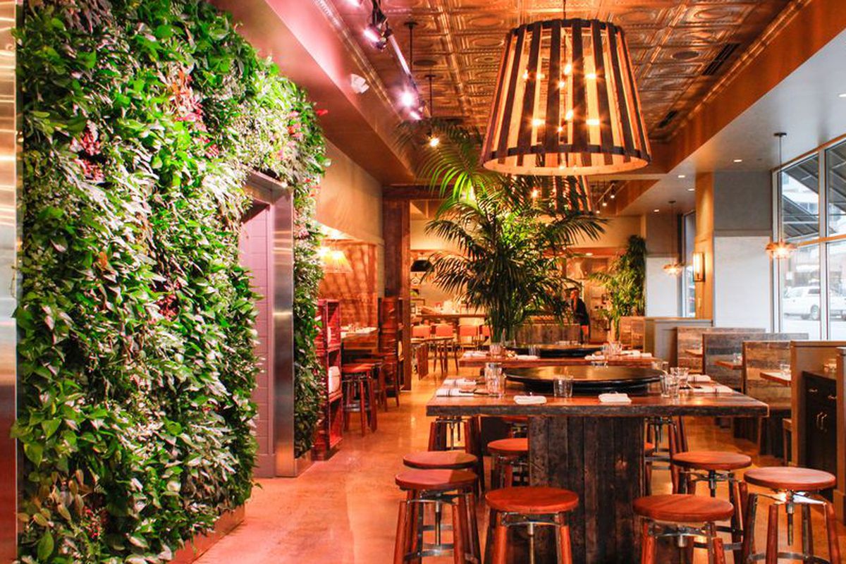 A colorful restaurant interior features orange and gold accents and a wall covered in green plants