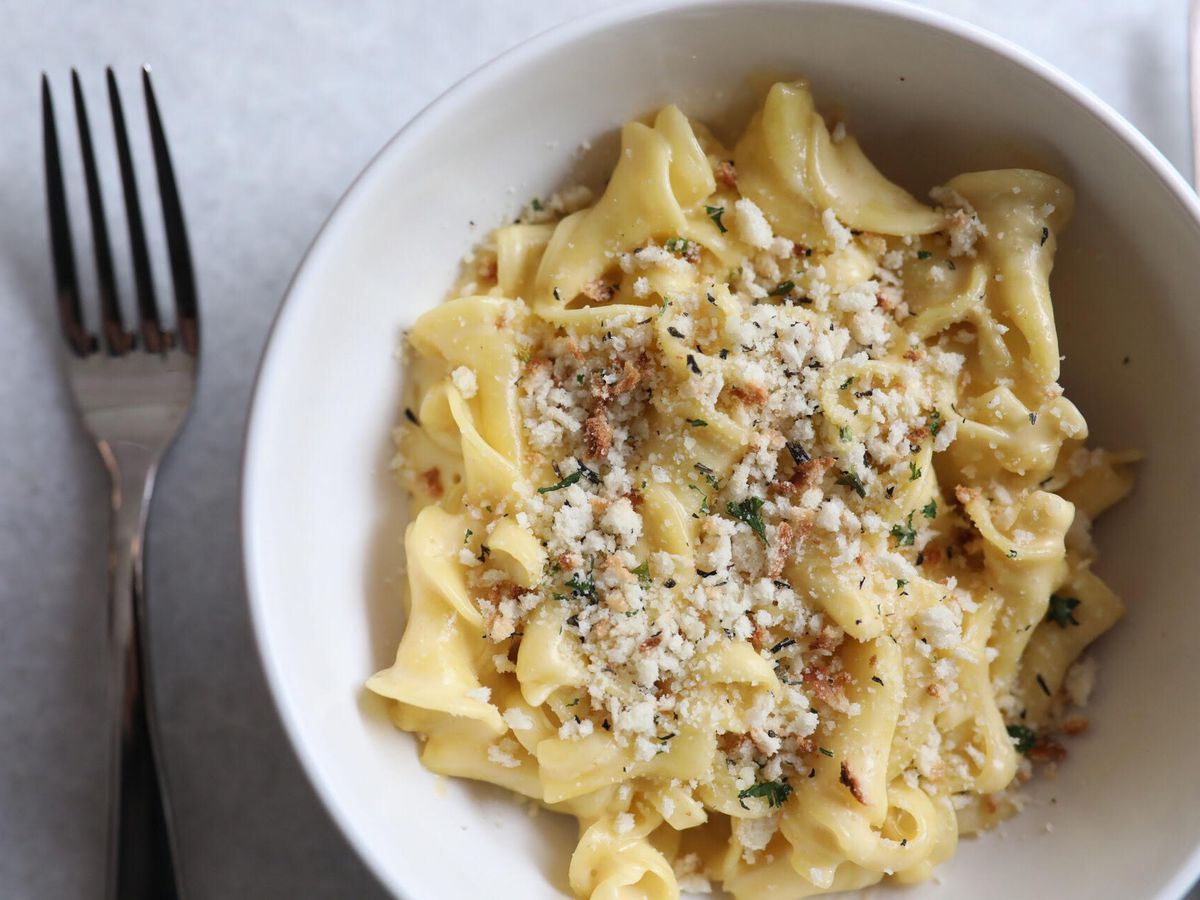 A white bowl holds egg pasta topped with crispy breadcrumbs
