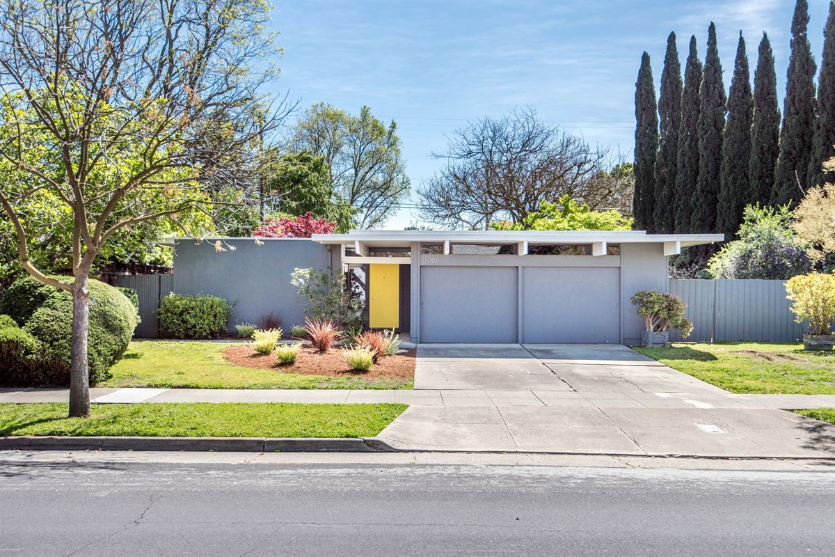 Midcentury, one-story Eichler with gray facade and bright yellow door.