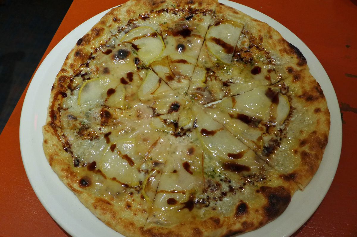 A yellowish round pizza with dark balsamic drizzled over it, on a red table...