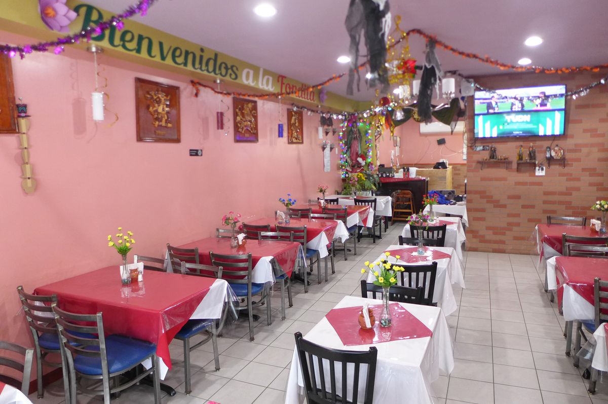 A dining room with black tables in two rows and pink walls, a sign up above reads Bienvenidos...