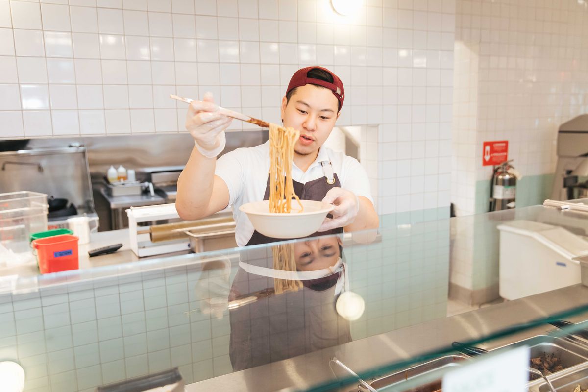 Lucas Sin uses chopsticks to add noodles to a bowl behind the counter at Junzi Kitchen.