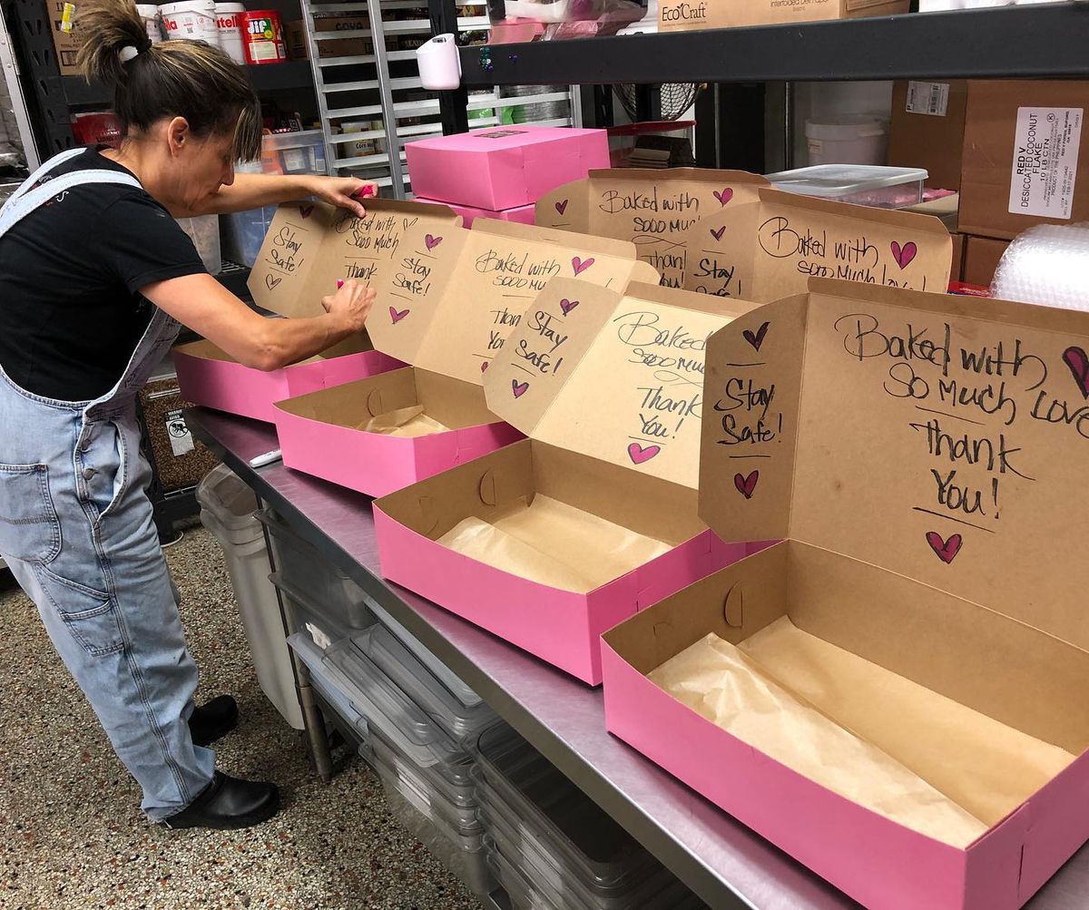 Kruse wearing a ponytail, a black shirt, and jean overalls packs bright pink to-go boxes with baked goods. 