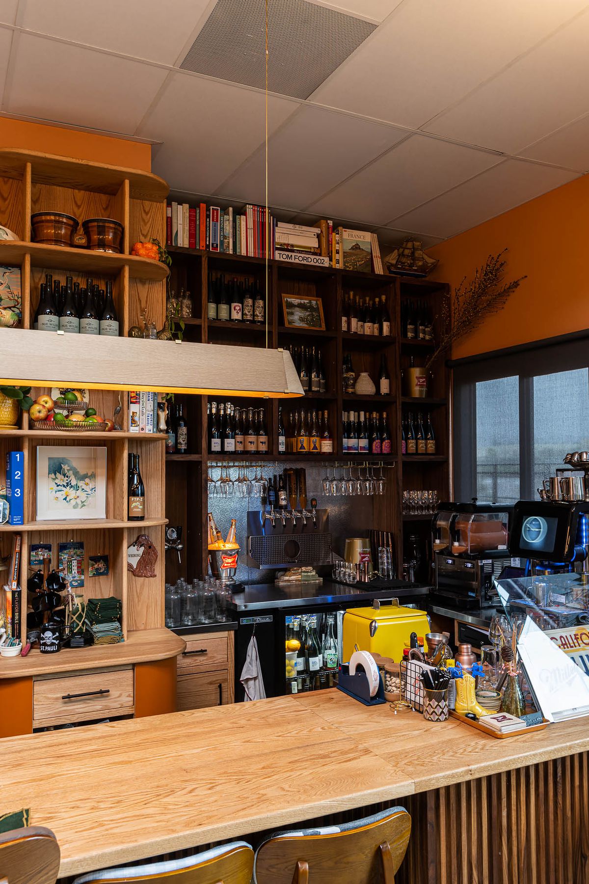 A service corner at a restaurant with tall bottles of wine on shelves, cookbooks, and small decor items.