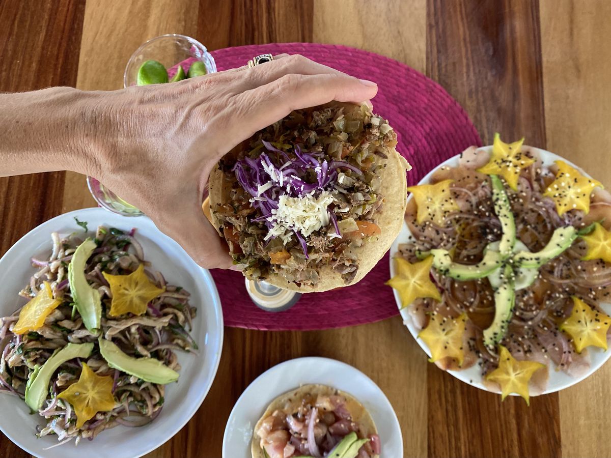 From above, a hand holds a tostada over a table set with other dishes
