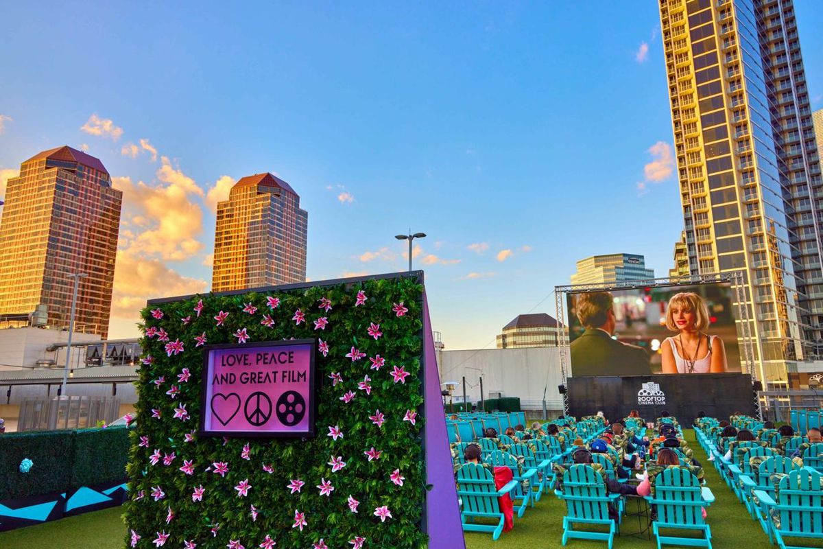 Rows of Adirondack chairs facing a large outdoor screen and the Uptown skyline.