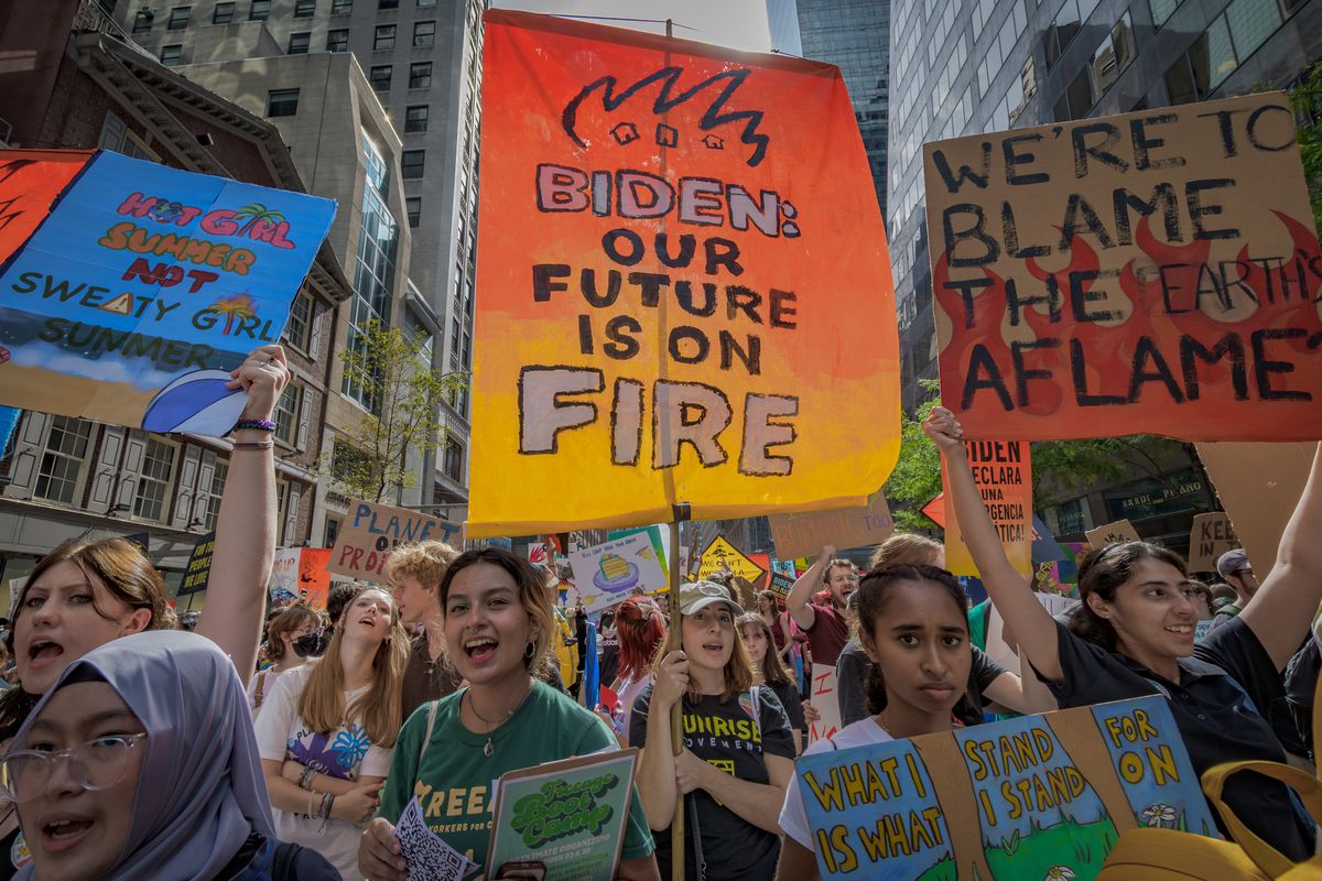 A group of protesters carrying signs, one of which reads “Biden, our future is on fire.”