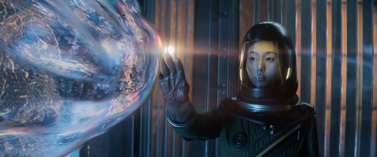 A woman in a spacesuit reaches out to touch a blob refracting light and seemingly coming toward her like it’s alive in Apple’s Invasion season 2