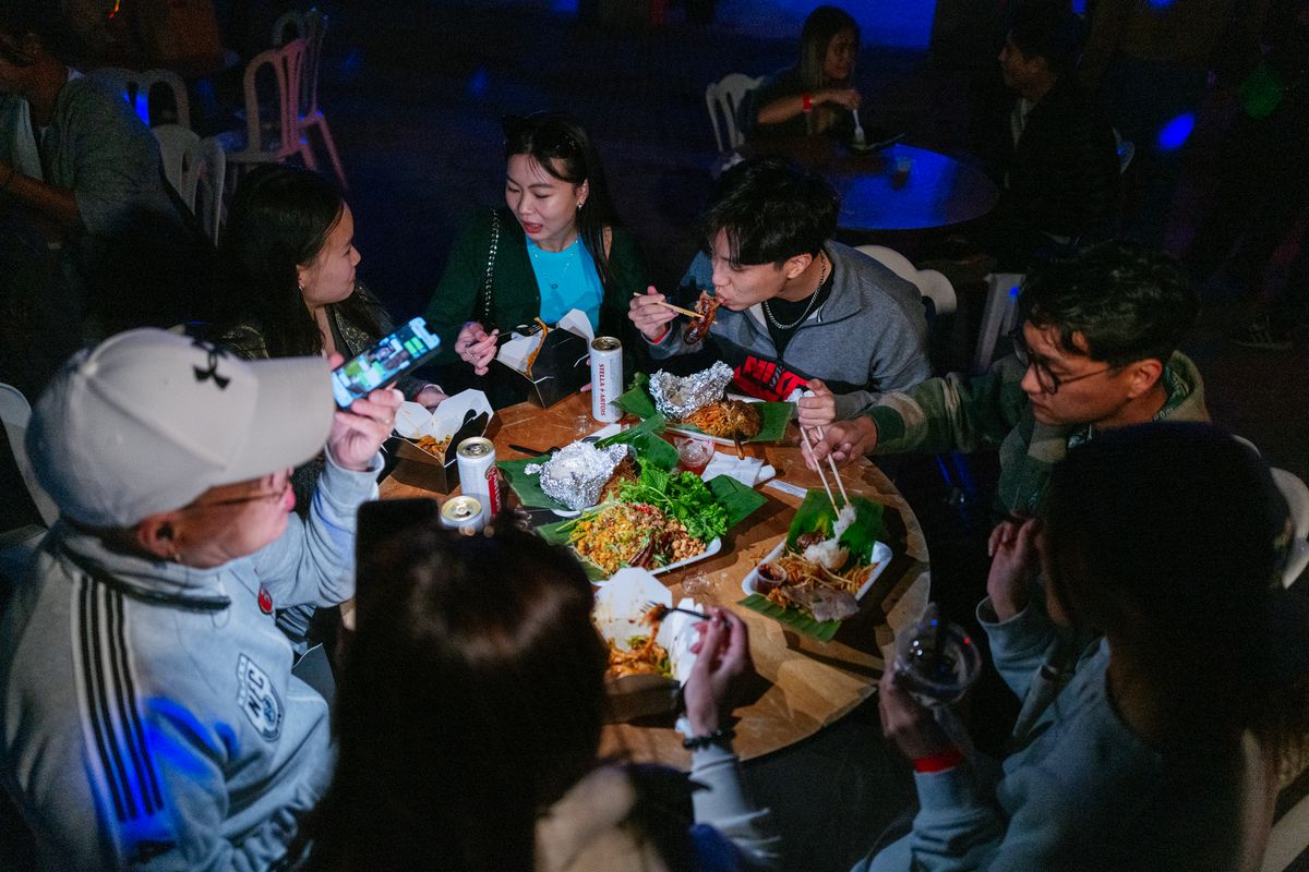 A group of people sit around a large wooden table filled with snacks.