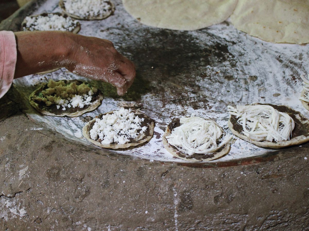 A woman’s arm reaches over a comal with cooking masa discs.
