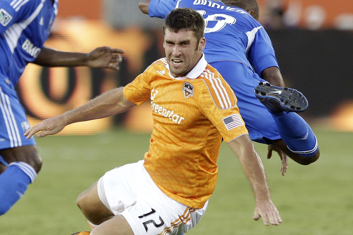 HOUSTON - JULY 21:  Will Bruin #12 of the Houston Dynamo takes a hard tackle from Collen Warner #18 of the Montreal Impact in the first half  at BBVA Compass Stadium on July 21, 2012 in Houston, Texas.  (Photo by Bob Levey/Getty Images)