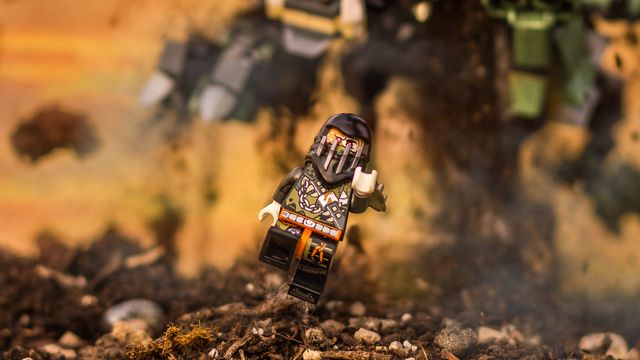 A ninja Lego minifig being chased by a lego-built monster flinging dirt in the air as its claw reaches forward