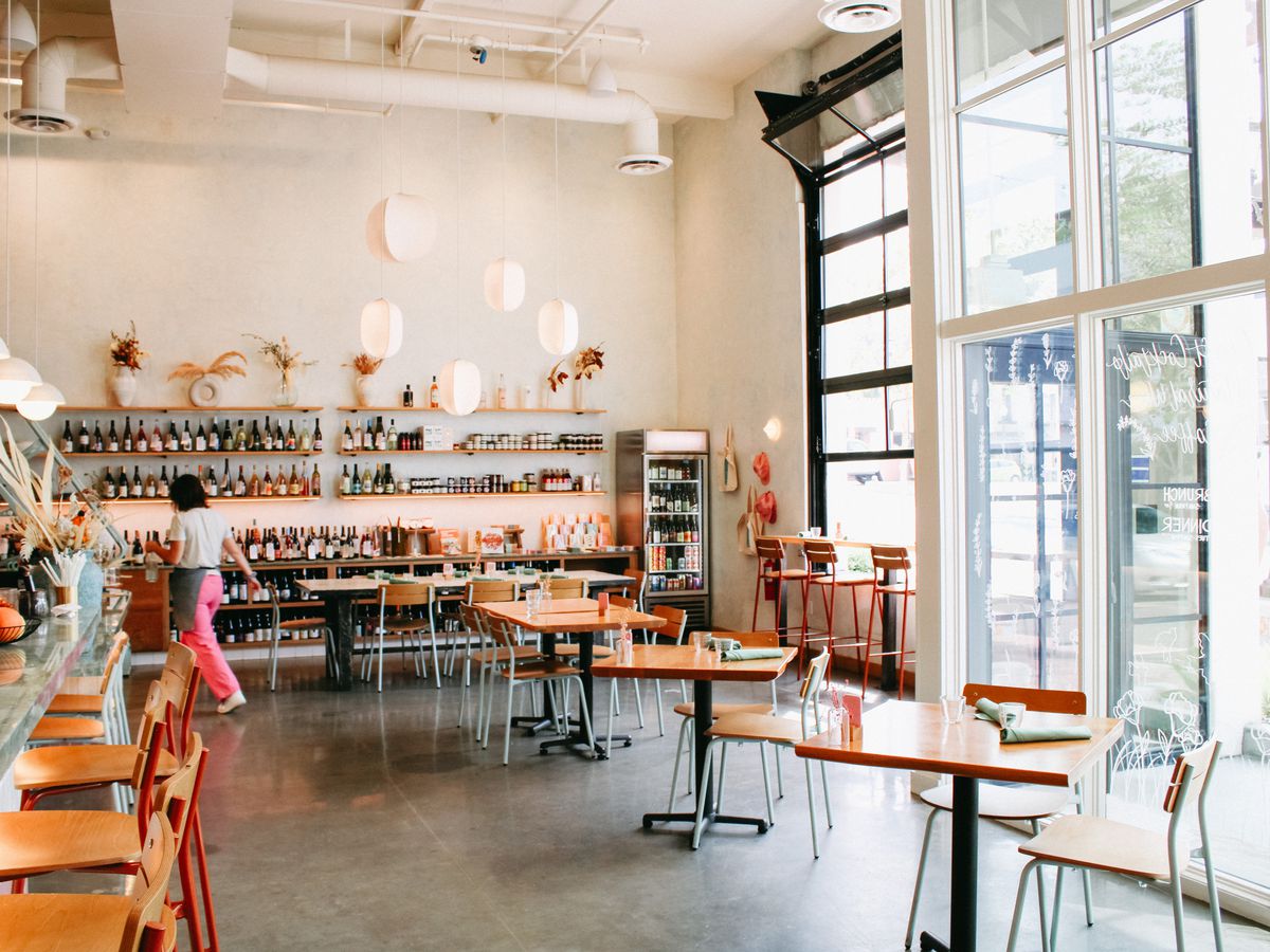 A light-filled coffee shop with wooden tables and colorful chairs.