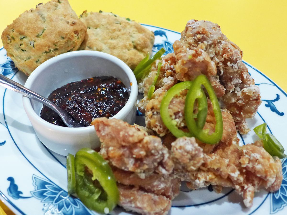 Fried chicken strewn with pickled jalapenos with a pair of biscuits in the background.